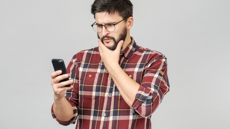 Mann schaut verwundert aufs Handy, weil Frau nicht zurückschreibt