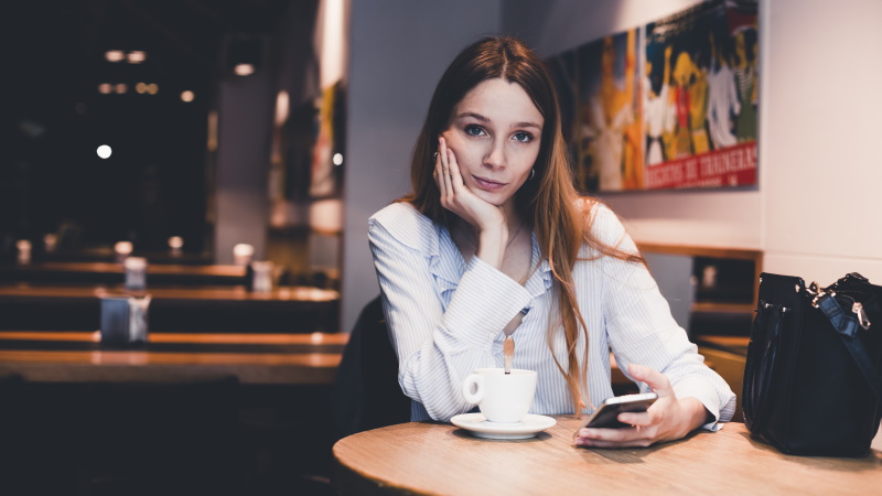 Frau mit Smartphone sitzt gelangweilt am Tisch