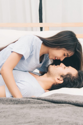 Frau beugt sich lachend über Mann im Bett zum küssen