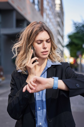 Frau schaut beim Telefonieren skeptisch auf ihre Armbanduhr