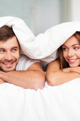 Frau und Mann sind zusammen unter Bettdecke und lächeln sich an