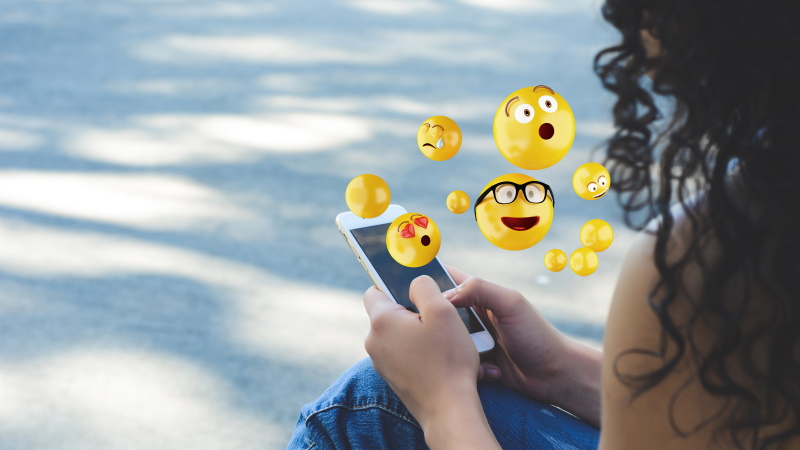 Frau, aus deren Handy gelbe lustige Smileys aufsteigen