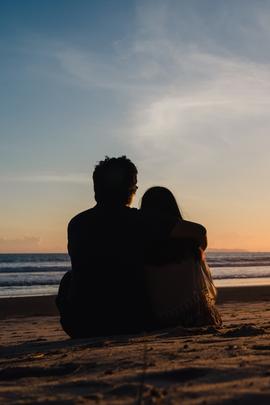 Mann und Frau sitzen umarmend am Strand