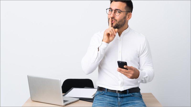 Mann mit Handy im Büro schaut geheimnisvoll