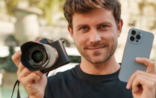 Lächelnder Mann hält Fotokamera und Smartphone in den Händen