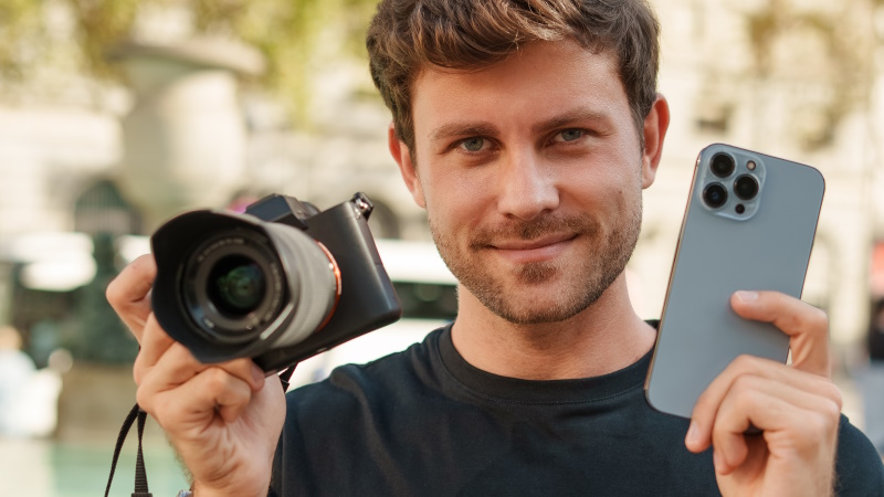 Lächelnder Mann hält Fotokamera und Smartphone in den Händen
