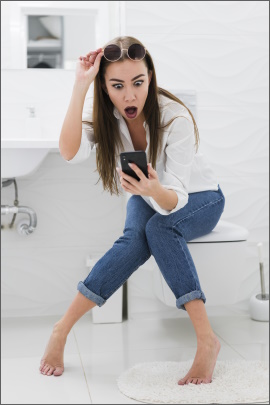 Frau sitzt auf dem Klo und schaut schockiert aufs Handy