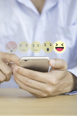 Mann mit Smartphone, über dem Emojis schweben