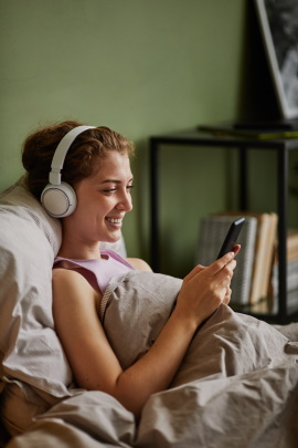 Frau liegt im Bett und schaut lächelnd aufs Handy
