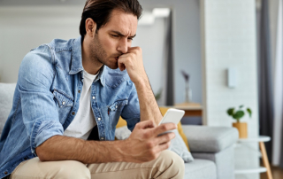 Mann sitzt auf dem Sofa und schaut verärgert aufs Handy