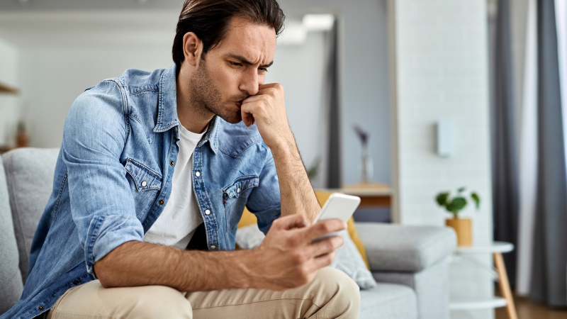 Mann sitzt auf dem Sofa und schaut verärgert aufs Handy