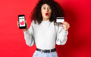Frau mit Handy und Kreditkarte schaut aufgeregt wegen Tinder-Kosten