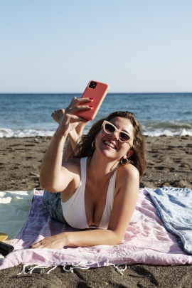 Lachende Frau mit Smartphone liegt am Strand