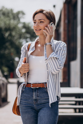 Lächelnde Frau läuft telefonierend durch die Stadt