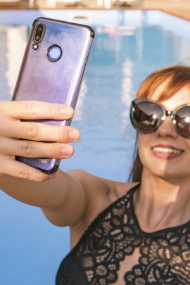 Frau mit Sonnenbrille macht Selfie am Swimming Pool
