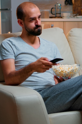 Mann mit Schüssel Popcorn sitzt gelangweilt vor dem Fernseher