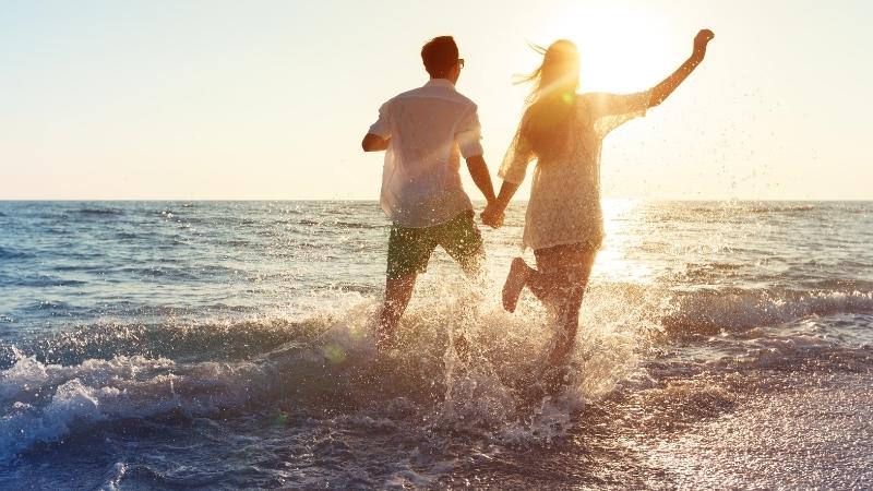 Mann und Frau halten Händchen und laufen am Strand entlang