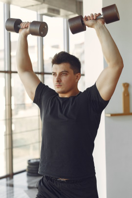 Mann steht im Fitnessstudio und hebt Hanteln