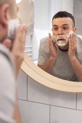 Mann steht vor Spiegel mit Rasierschaum im Gesicht