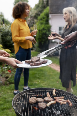 Leute stehen im Garten am Grill und reden miteinander