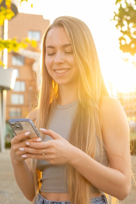 Frau bei Dämmerung schaut lächelnd aufs Handy