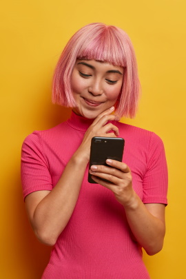 Frau mit rosa Perücke schaut lächelnd aufs Handy