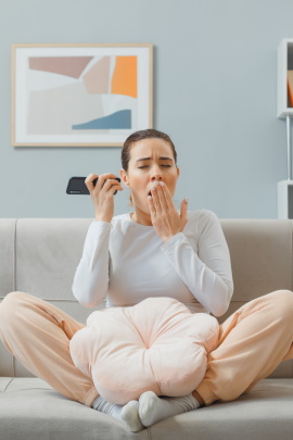 Frau mit Smartphone sitzt gähnend auf dem Sofa