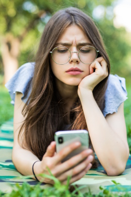 Frau liegt auf der Wiese und schaut kritisch aufs Smartphone