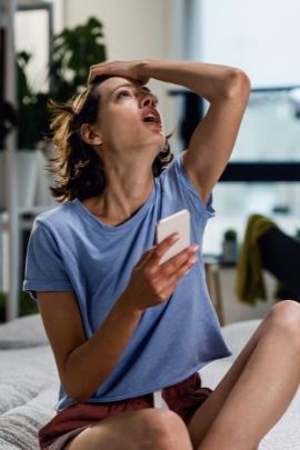 Frau hält ihr Handy in der Hand und schaut fassungslos nach oben