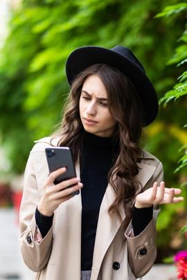 Frau schaut verdutzt auf ihr Smartphone, weil Chatpartner sich komisch verhält