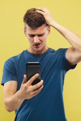 Mann schaut skeptisch aufs Handy und streicht sich durchs Haar
