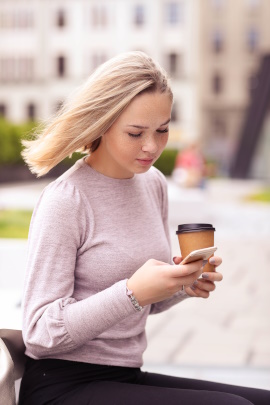 Frau läuft mit Kaffeebecher und Handy durch die Stadt