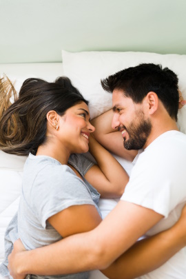 Paar liegt im Bett und schaut sich lächelnd an