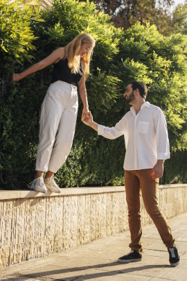 Mann führt Frau, die auf der Mauer läuft, an der Hand