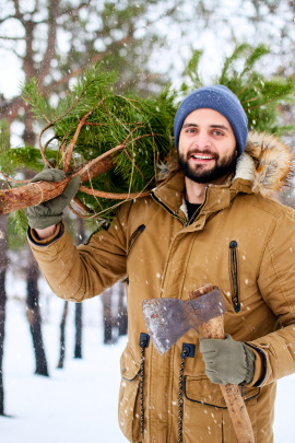 Mann mit Axt trägt Nadelbaum durch den Wald im Winter