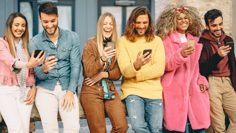 Gruppe fröhlicher Menschen mit Smartphones steht vor einer Wand