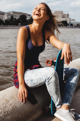 Frau mit Skateboard sitzt am Ufer eines Flusses