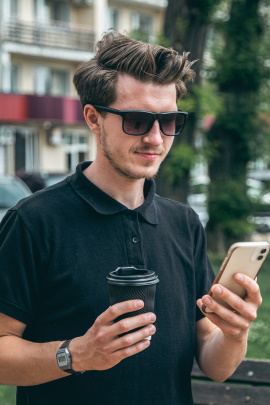 Mann mit Sonnenbrille und Kaffeebecher schaut aufs Handy