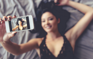 Lächelnde Frau liegt auf dem Bett und macht ein Selfie