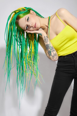 Schrille Frau mit grünen und gelben Haaren neigt den Kopf zur Seite