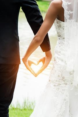 Mann und Frau in Anzug und Brautkleid formen ein Herz mit ihren Händen