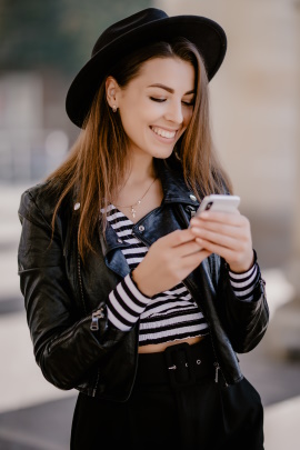 Frau mit Hut schaut lachend aufs Smartphone