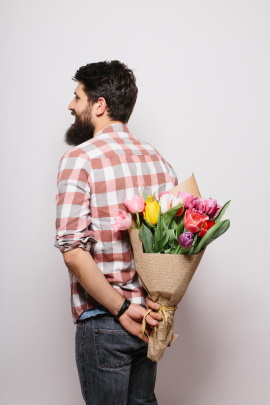 Mann hält Blumenstrauß hinter seinem Rücken