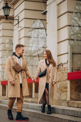 Mann und Frau im Mantel laufen Händchen haltend am Gebäude vorbei