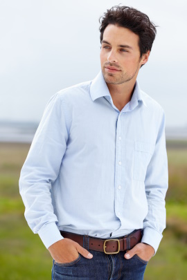 Mann im hellblauen Business-Hemd mit Jeans steht auf einer Wiese