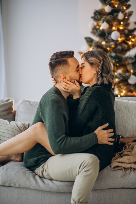 Paar sitzt küssend auf dem Sofa vorm Weihnachtsbaum