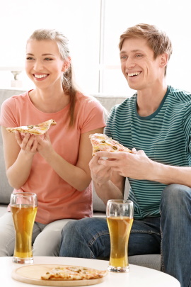 Paar sitzt bei Bier und Pizza vor dem Fernseher