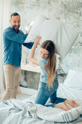 Lachendes Paar auf dem Bett bei einer Kissenschlacht