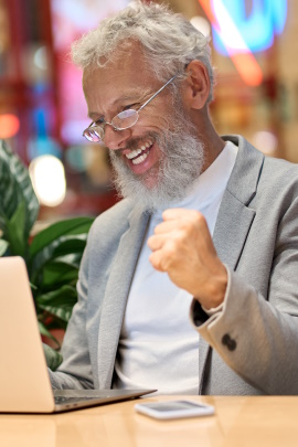 Alter Mann mit Bart schaut jubelnd auf den Laptop